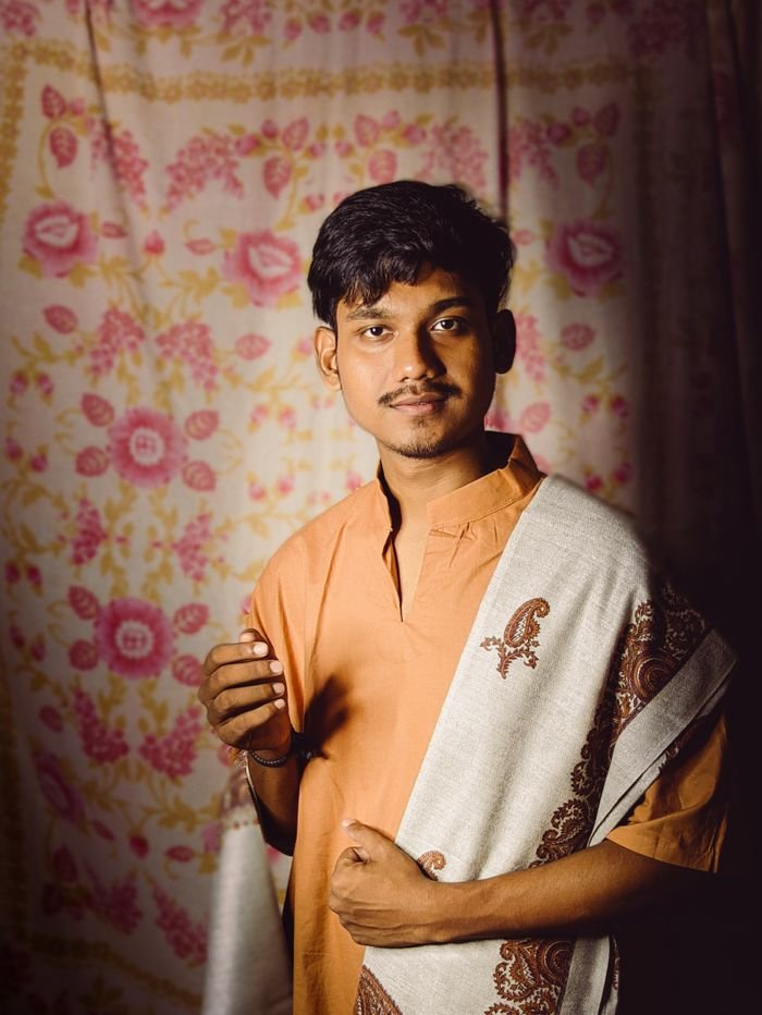 Portrait of a young Indian man wearing traditional attire with a patterned shawl, indoors.