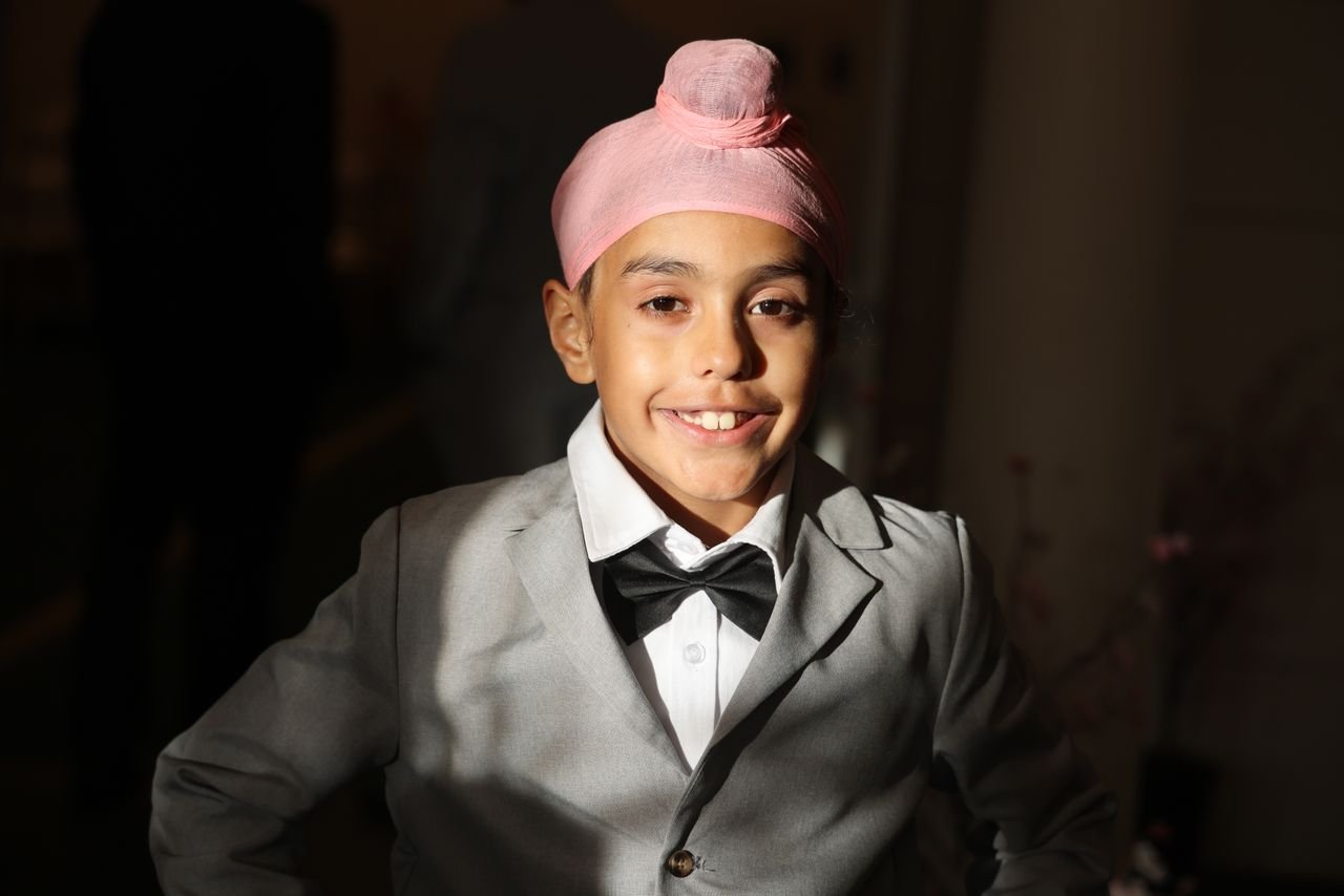 Smiling boy wearing a suit and pink turban. Elegant and cheerful expression captured indoors.